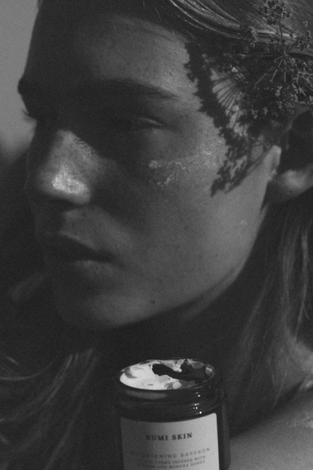 Person with a jar of 'Rumi Skin' product on a dark background