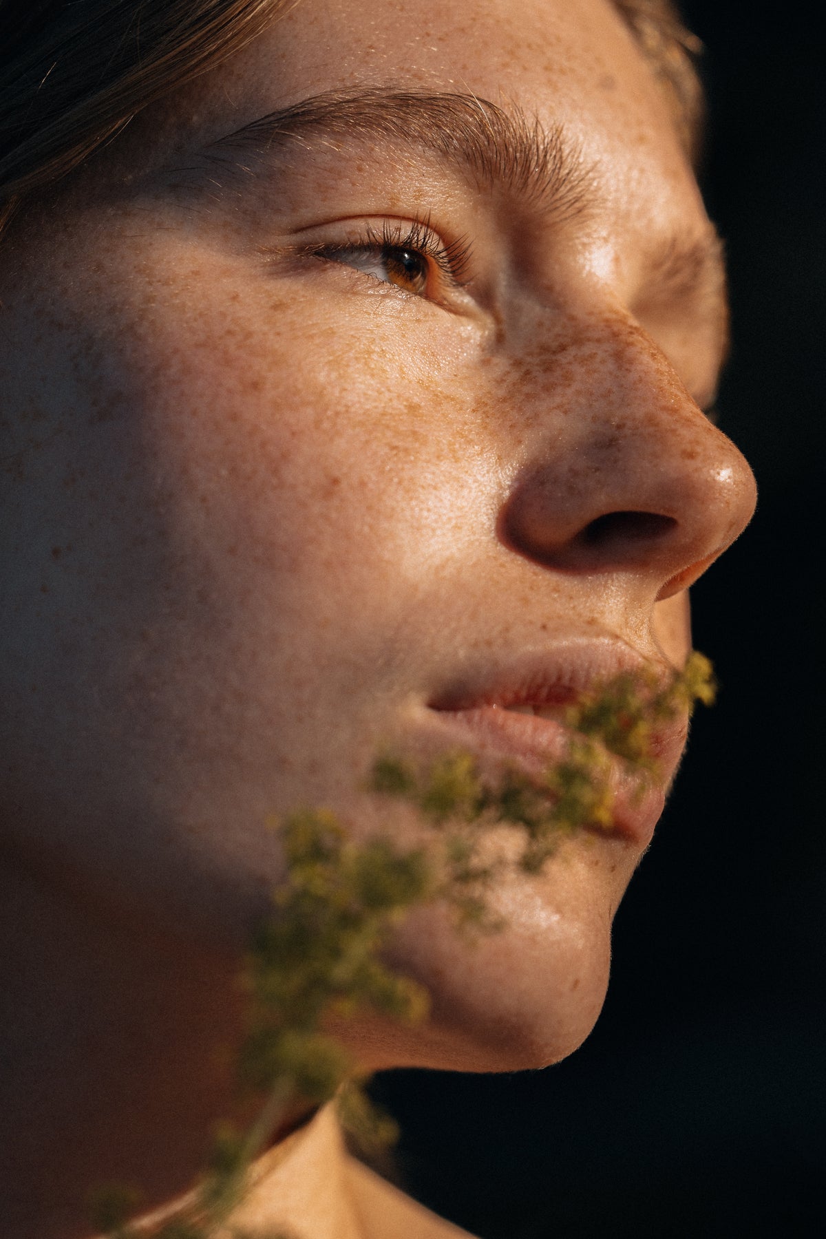 Close-up of a person with a plant near their mouth against a dark background