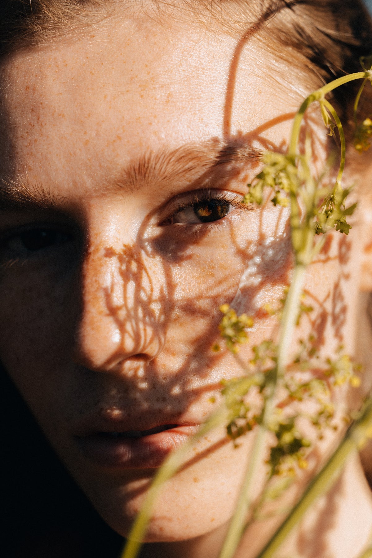 Close-up of a person's face with plant leaves casting shadows over their eyes.